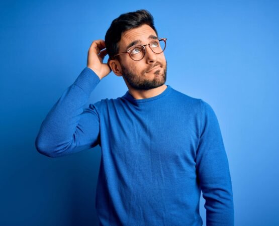 Young handsome man with beard wearing casual sweater and glasses over blue background confuse and wondering about question. Uncertain with doubt, thinking with hand on head. Pensive concept. Young handsome man with beard wearing casual sweater and glasses over blue background confuse and wondering about question. Uncertain with doubt, thinking with hand on head. Pensive concept.
