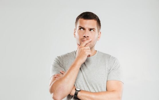 Thinking young man looking aside. Image of concentrated thinking young man dressed in grey t-shirt isolated over grey wall background. Looking aside.